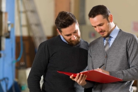 Zwei Männer stehen beisammen und besprechen einen Folder