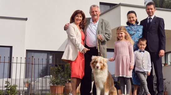 Großfamilie steht beisammen vor Eigenheim